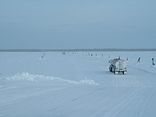 Véhicules qui traversent la rivière Albany, sur la route d'hiver allant de Moosonee à Attawapiskat au Nord de l'Ontario, Canada. Le bord de la route est marqué par de petits arbres. Les véhicules lourds doivent maintenir un espacement large et une vitesse lente.