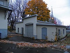 Un garage près d'un autre bâtiment, de plan complexe, revêtu de brique beige.