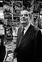Photo en noir et blanc d'un homme d'environ 80 ans, devant des magazines dans un kiosque à journaux.