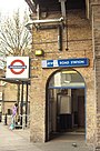 A beige-bricked building with a dark-blue, rectangular sign reading "LATIMER ROAD STATION" in white letters all under a white sky