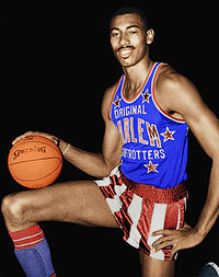 Черный мужчина стоит на коленях на одном колене с баскетбольным мячом на другом, а его рука на баскетбольном мяче. Он одет в красно-бело-синюю униформу Harlem Globetrotters.