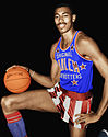 A photograph of a man in a blue uniform and red and white shorts palming a basketball