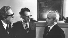 Three men in suits stand in a semi-circle. The two on the left, Jimmy Allen and Marc Tanenbaum, are facing the man on the right, Frank Reynolds. The three are engaged in conversation.