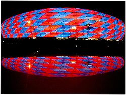 Photographie d'un stade de football, vu de l'extérieur, avec des couleurs rouges et bleues.