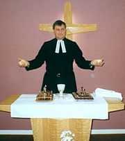 A minister, dressed in a cassock and preaching bands, presides over a service of Holy Communion Methodist Communion.jpg