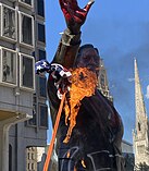 A statue of Frank Rizzo that has been spray-painted and that has a burning American flag attached to it with a rope