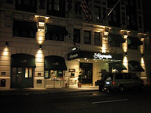 Точечные светильники подчеркивают каменный фасад отеля и арочные окна магазинов с навесами. Вход в отель закрывается большим навесом.