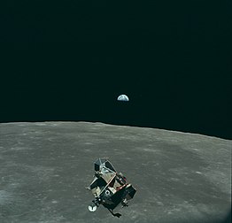 Le module lunaire d'Apollo 11, le 21 juillet 1969, de retour de l'exploration lunaire, avant l'arrimage, avec la Terre en arrière-plan. La planète Mars est également visible sur la photographie (point rouge à droite de la Terre). (définition réelle 4 170 × 4 007)