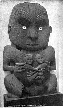 A wooden Māori carving of a person holding two smaller people, who appear to be holding each other.