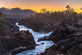 Cascades de Li Phi (chutes de Khone) au crépuscule avec un ciel jaune orangé.