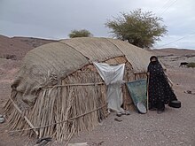 عکس از پیرزن محلی در حوالی شهرستان رودبار جنوب که کنار خانه کپری خود ایستاده است.- سال ۲۰۱۲ میلادی (دریافت تصاویر رایگان با کیفیت بالا از انبار ویکیپدیا)