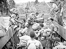 Black and white photograph of a group of men with military equipment, including rifles and packs, in an open-topped boat