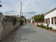 Une rue de village bordée de maisons basses à toits de tuiles canal et façades peintes blanc ou murs en pierre.