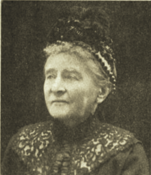 B&W portrait photo of an elderly woman with her hair in an up-do, wearing a dark hat and dark blouse.