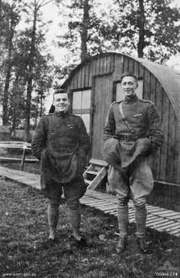 Deux hommes en uniforme militaire se tiennent côte à côte. L'homme de gauche est petit et trapu, celui de droite est grand et mince. À l'arrière-plan se trouve une cabane.