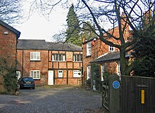 A cobbled courtyard with brick buildings on three sides, some of them timber-framed. On the gatepost on the right is a blue commemorative plaque