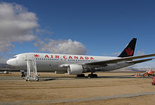 Вид сбоку на припаркованный двухмоторный реактивный самолет Air Canada в пустыне с лестницей, установленной рядом с передней дверью самолета.