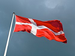 A Danish flag flies from a flagpole against the sky.