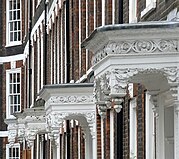 A row of ornate white porches hanging out from dark red brick houses.