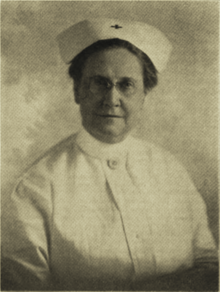 B&W portrait photo of a woman wearing a white nurses hat and uniform.