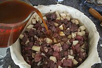 Versage du bouillon dans une tourtière constituée de chevreuil et d'orignal. La cuisson durera plusieurs heures.