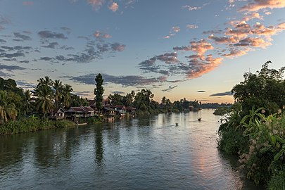 Habitations et pirogues sur la berge de Don Det, au lever du soleil avec des nuages roses, vus depuis le pont de Don Khon. Décembre 2021.