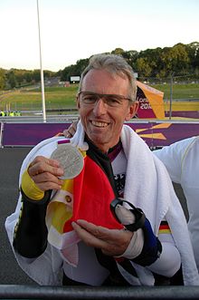 Man with glasses draped in a German flag holding up a silver medal.