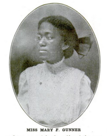 A young Black woman wearing a white dress with a hair bow