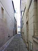 Photographie en couleurs d'une étroite rue pavée, vue en enfilade entre deux deux rangées de façades.