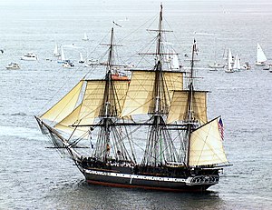 Constitution sailing in Massachusetts Bay with six sails set and a crowd of civilian boats in the background with passengers aboard observing