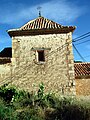 Vista de construcció tradicional a Esbiaixa, Ademús, amb detall de l'arrebossat amb morter de calç als murs, escaires de carreuat travat i coberta a quatre aigües, de l'església parroquial. S. XVI-XVII