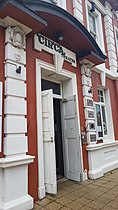 doorway from the outside of the building taken from an angle, the doors are open. white wood and red painted brick and stone work. a sign above the door says Circa Theatre