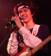 Conan Gray with a guitar, smiling and holding a microphone