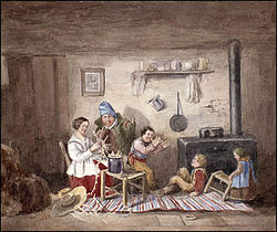 Early settler habitant family - mother, father, three children - gathered together in their one-room home in front of the cast iron cooking stove. The mother appears to be knitting and the children playing a game..