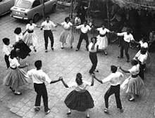 A circle of people, dressed in traditional Catalan clothing, dance in a circle holding hands.