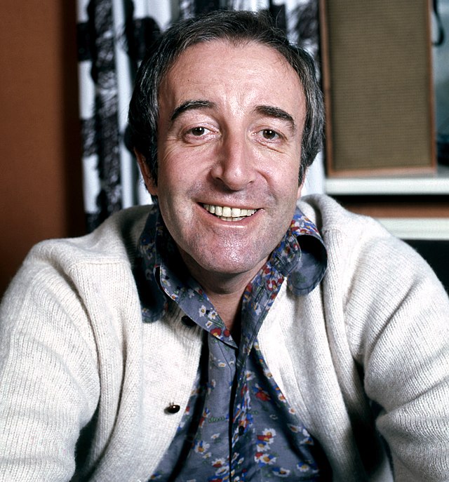 A head and shoulder shot of a smiling man wearing a white cardigan