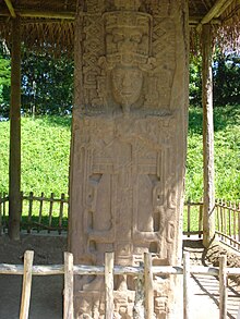 Un cercu cola prominente escultura d'un rei arrodiáu de decoración ellaborada. El monumentu ta cubiertu por un techu de paya sosteníu por postes de madera.