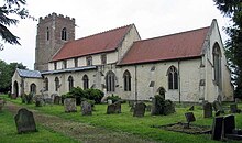 A stone church with red tiled roofs seen from the southeast, showing a battlemented tower, a nave with a clerestory, a south porch and a chancel