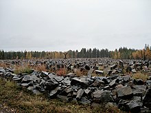 Тысячи разбросанных камней усеивают пейзаж. Вдалеке медленно желтеют листья деревьев. Это место памятника Зимней войне в Суомуссалми, Финляндия, содержащее камень для каждого солдата, погибшего в битве при Суомуссалми: 750 финнов и примерно 24 000 советских.