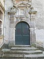 porte en bois à deux battants sous une arche portée par des pilastres. Le dessus est surmonté d'un fronton.