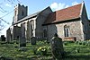 A stone church seen from the southeast, showing a chancel with a red tiled roof, a much larger nave with a slated roof, and a battlemented tower