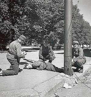 Lääkintämiehiä antamassa ensiapua taistelussa haavoittuneelle sotilaalle. Kuva lavastettu.