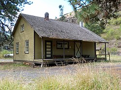 Photograph of a wooden building with a porch/loading dock and steep, rocky slopes in the background.