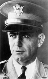 Facial shot of a cleancut middleaged uniformed man in dress hat with face turned quartering toward left side of shot
