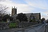 Side view of a long stone-built church set in a churchyard behind a low wall, with a tower to the left.