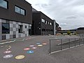 Nybygget fra 2012 på Lunde barneskole ligger midt i mot arkitektene Brochmanns fredede skolebygg fra 1950-tallet – med skolegården i mellom. Foto: Bxrzoi (2022)