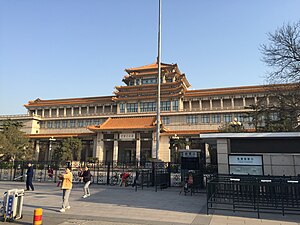 An ornate building front stretching the width of the image, slightly tilted, against a uniformly blue sky. Its front has a projecting pavilion in the Chinese style, echoed by a similar pagoda-style top on the roof above it.