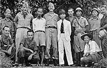 Photo en pied d'un groupe d'hommes, blancs et asiatiques, en uniforme ou en civil, debout face à l'objectif.