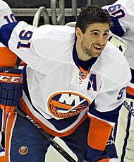 John Tavares wearing an away Islanders jersey with an assistant captain "A" on it while holding his hockey stick on the ice