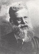 Portrait d'un homme âgé avec lunettes et grande barbe blanche ; tête légèrement inclinée.